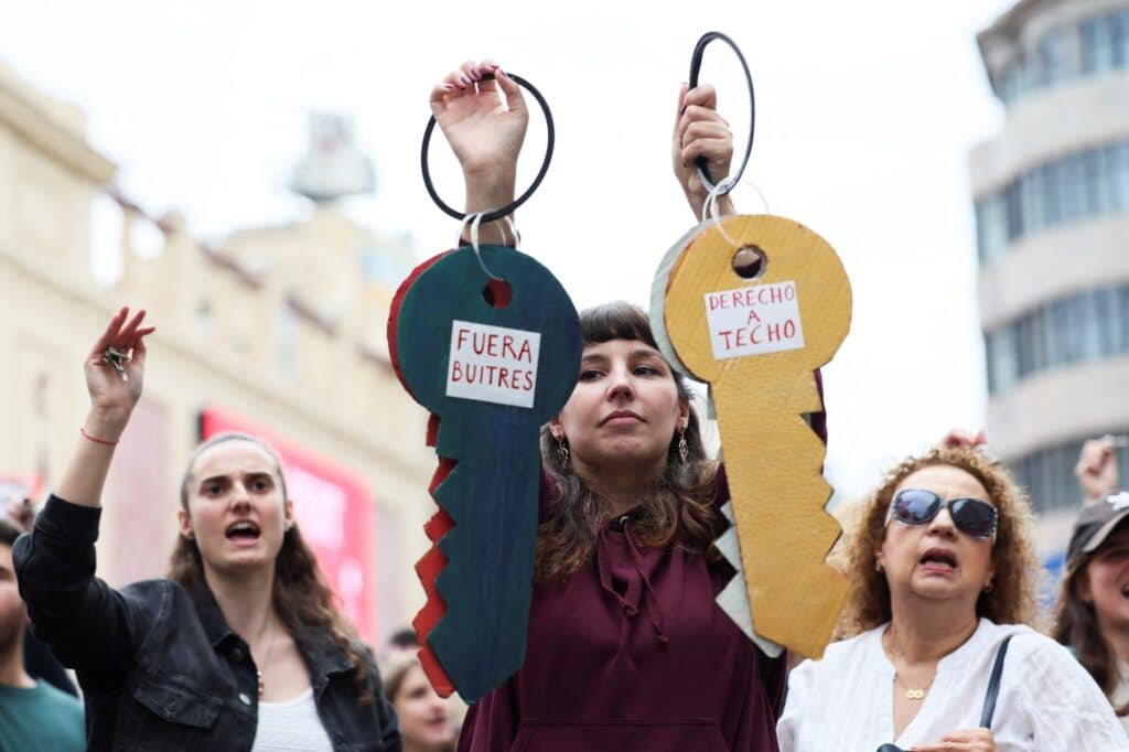 Žena drží kartonové klíče s nápisy „Pryč se supy“ a „Právo na střechu (nad hlavou)“